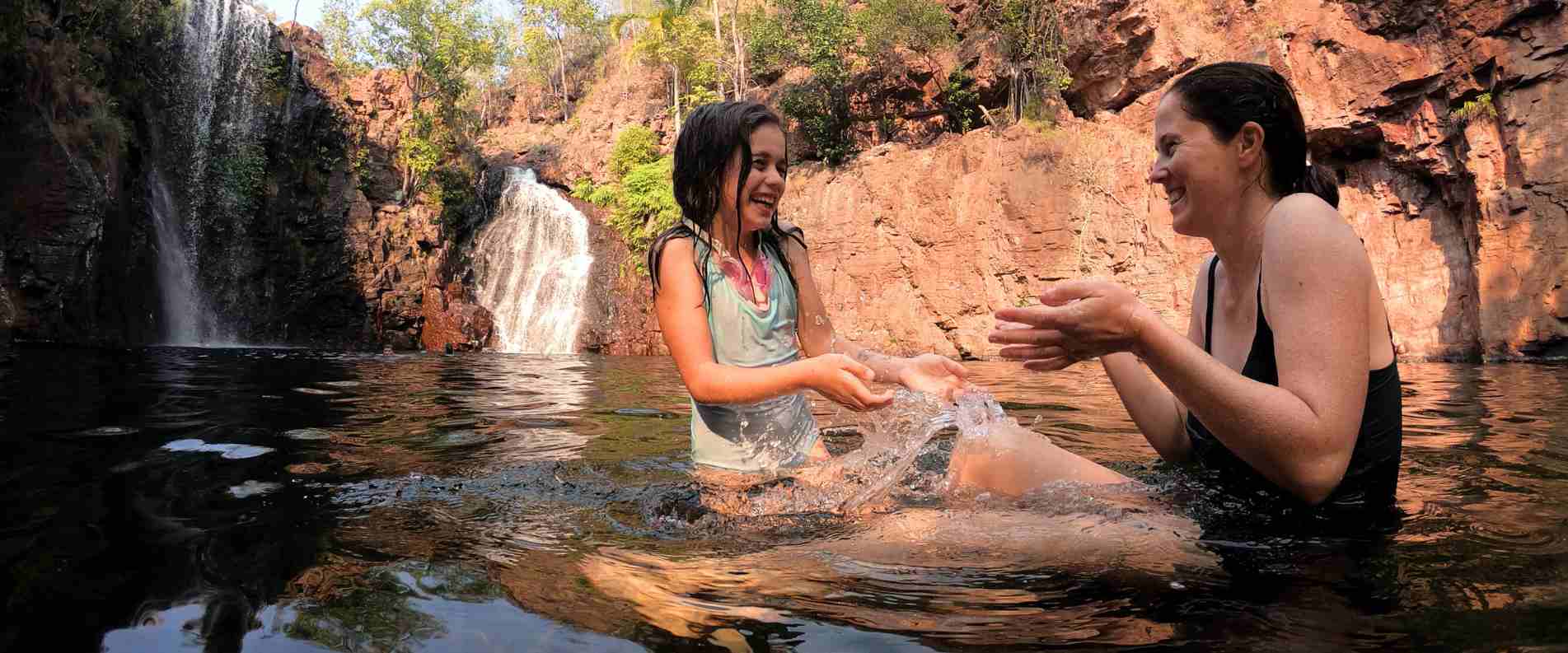 Mother and daughter sitting down playing in water in a swimming hole in the Northern territory 